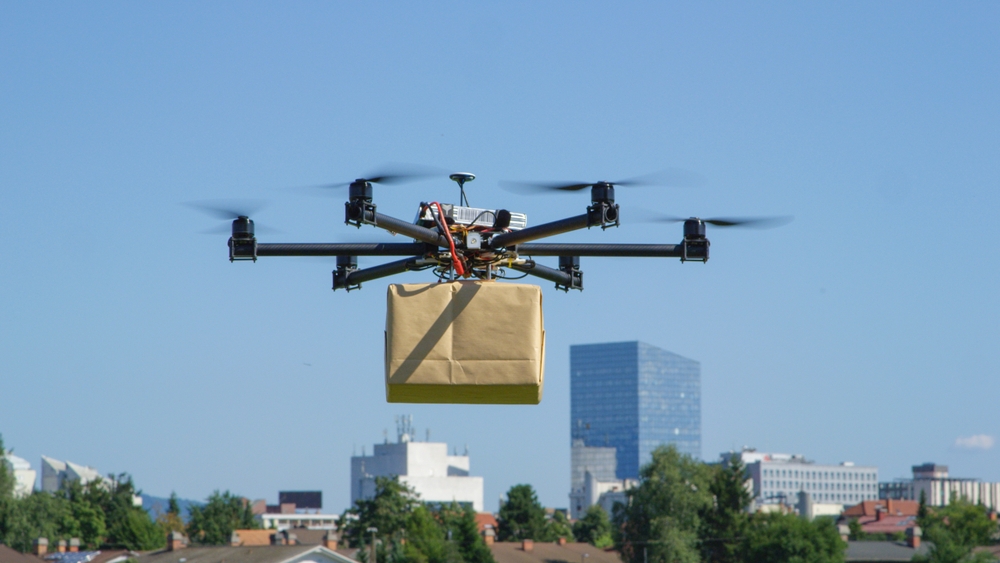 unmanned aerial vehicle with six rotors carrying box wrapped in brown paper hovering above city