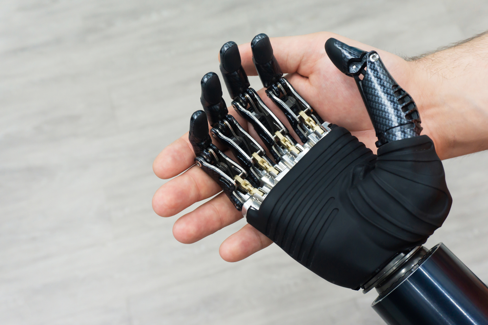 A black bionic, robotic, prosthetic hand. Behind the prosthesis is a human hand.