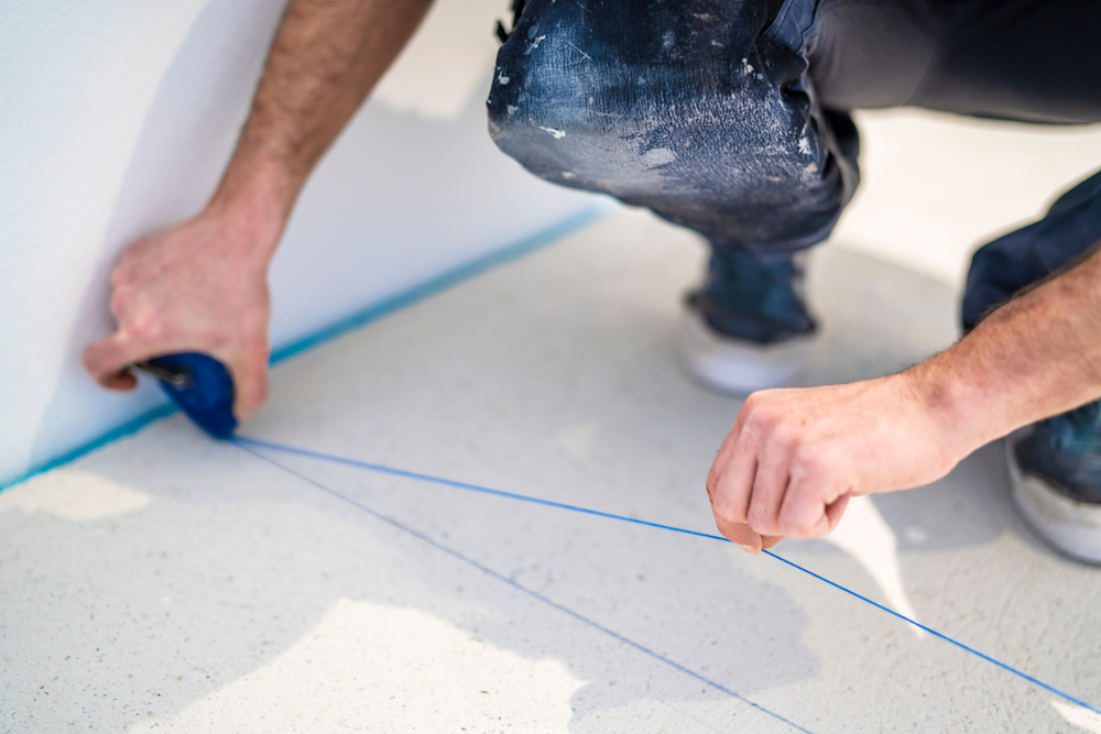 A chalk line about to be snapped onto a concrete floor by a construction workers hands